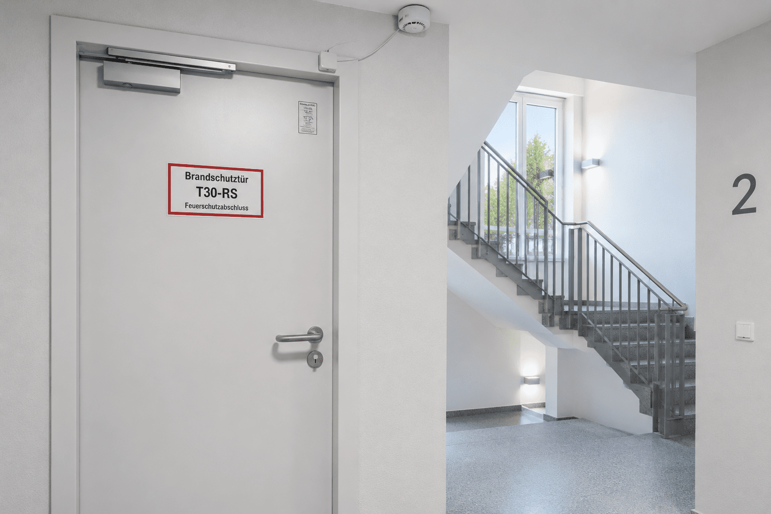 Moderne T30-RS Brandschutztür mit Kennzeichnungsschild und Rauchmelderkontakt in einem hellen Treppenraum gemäß DIN 4102 Brandschutz.