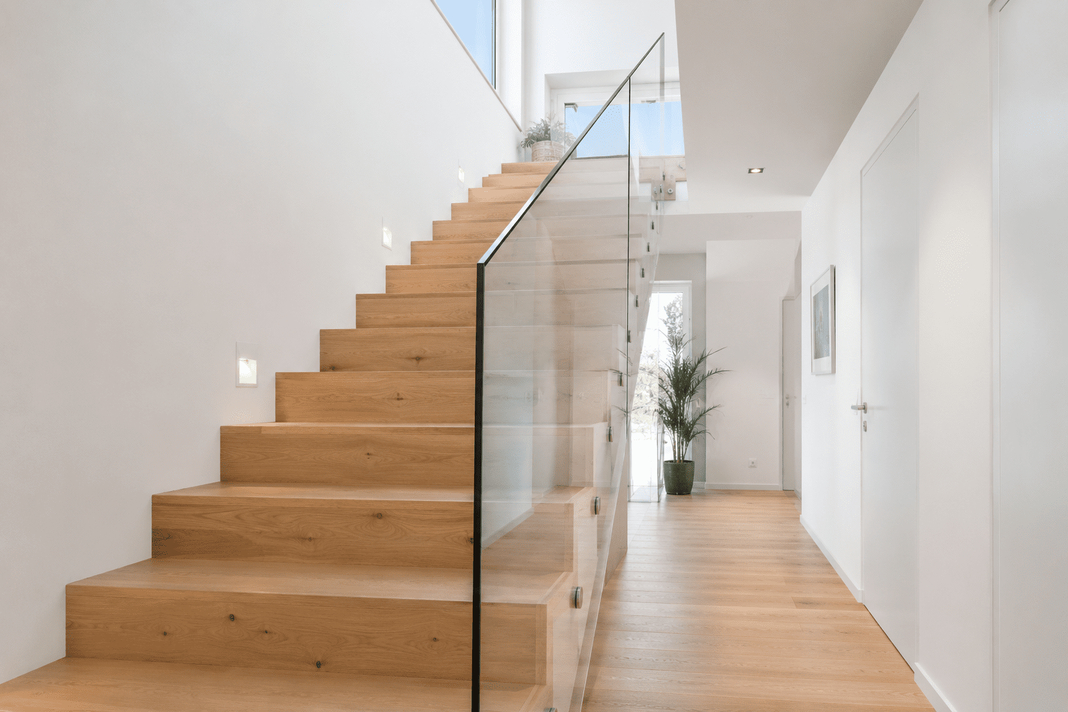 Moderne Eiche-Holztreppe mit minimalistischem Glasgeländer in einem hellen Wohnhaus gemäß DIN 18065 für sichere und komfortable Treppenanlagen.