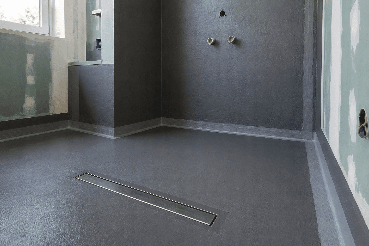 Frisch abgedichtete bodengleiche Dusche mit Dichtschlämme, Linienablauf und Dichtband nach DIN 18534 im Badezimmer-Rohbau.