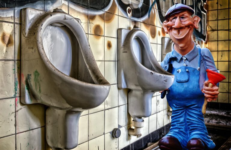Witzige Klempner-Figur mit Saugnapf neben Urinalen – Symbol für die Verwechslung zwischen Klempner und SHK-Fachmann
