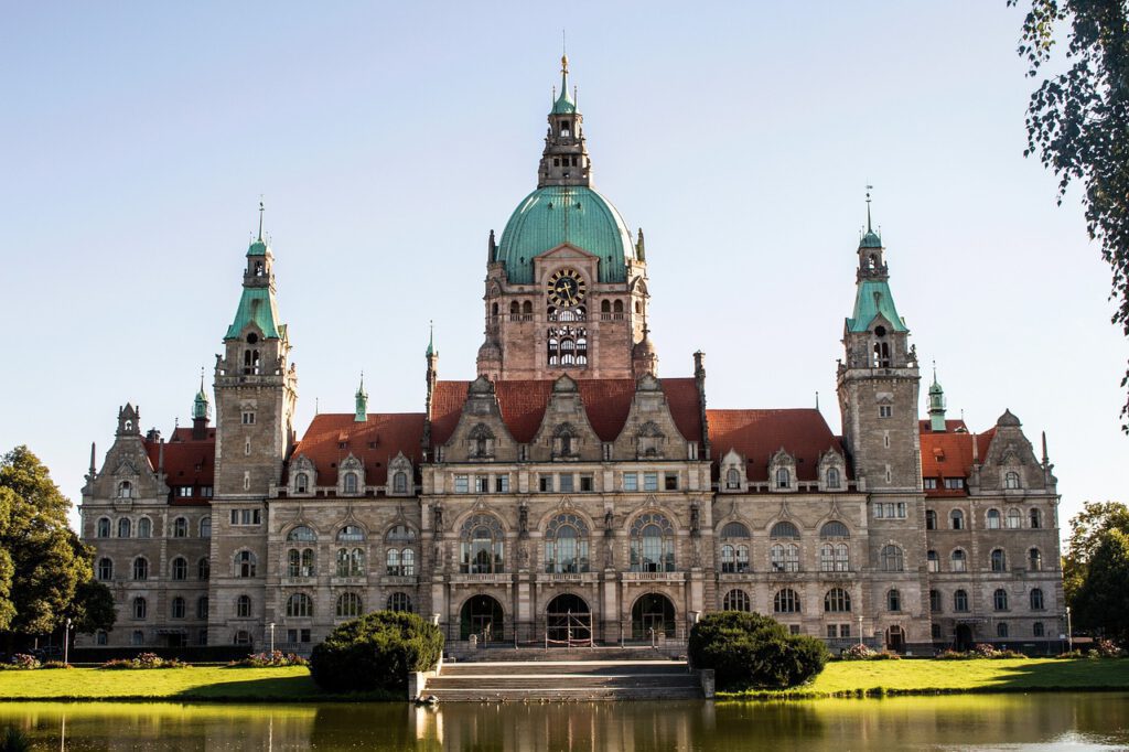 Neues Rathaus Hannover von der Parkseite mit Spiegelung im Maschteich, umgeben von Grünflächen, als symbol für Hausbau Region Hannover.