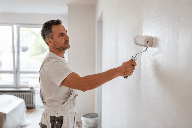 Maler streicht eine weiße Wohnzimmerwand mit Farbrolle – Malerarbeiten Kosten pro Quadratmeter im Innenbereich.